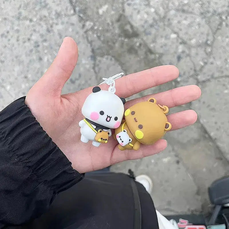 Hand holding Bubu and Dudu couple keychain with panda and bear figures on a textured surface.